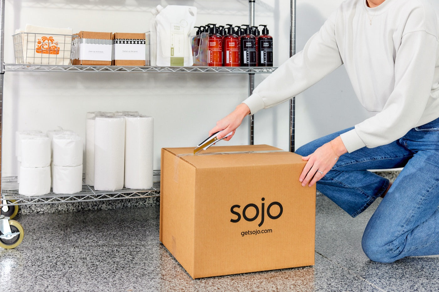 Person opening a sojo delivery box next to stocked shelves