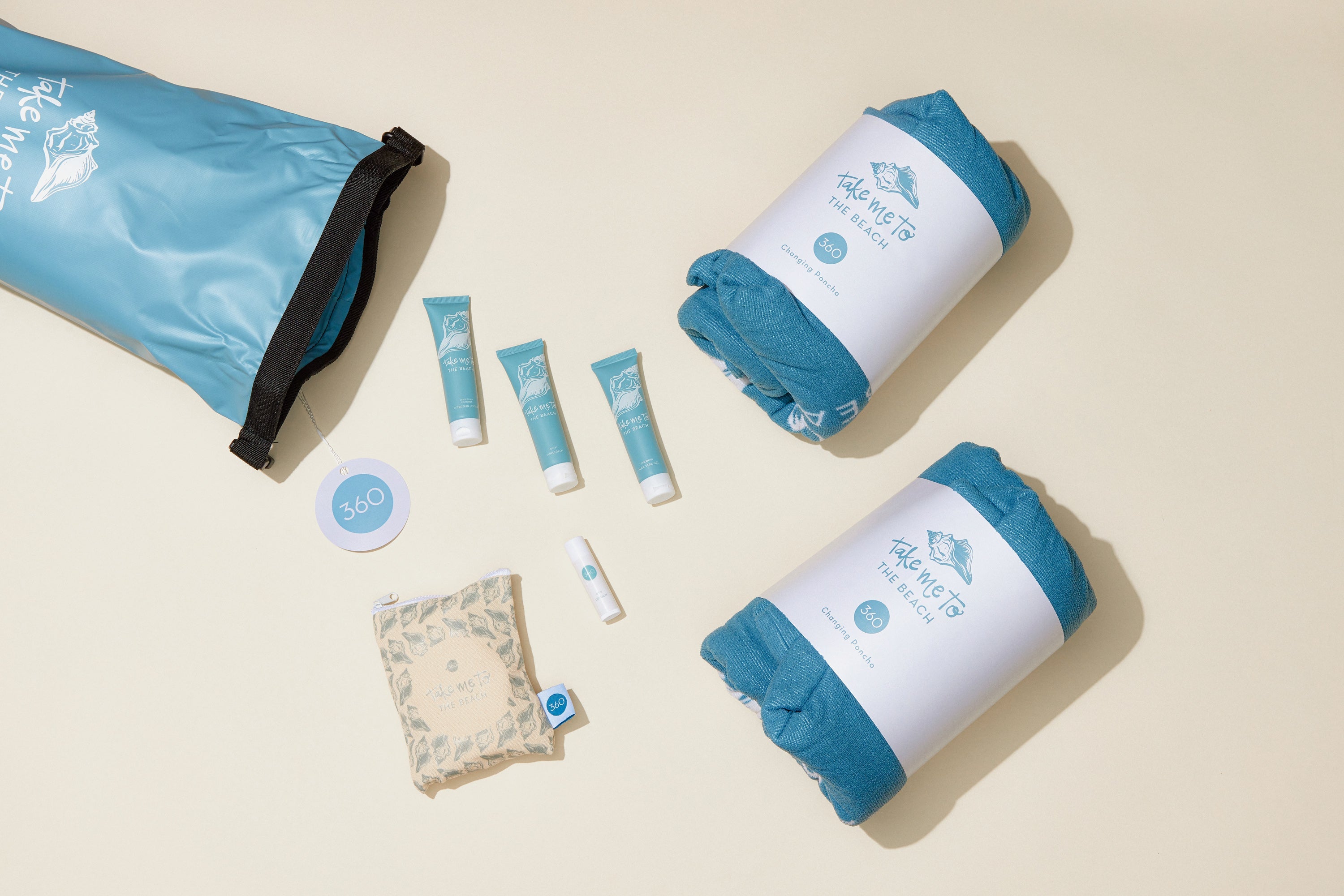 Beach guest gift set with blue towels, pouch, skincare tubes, and dry bag on beige background