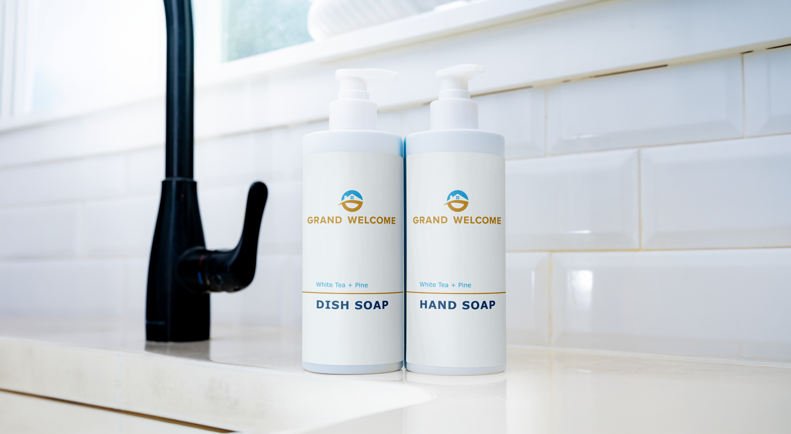 Two Grand Welcome refill bottles for dish soap and hand soap on a kitchen counter by a black faucet.