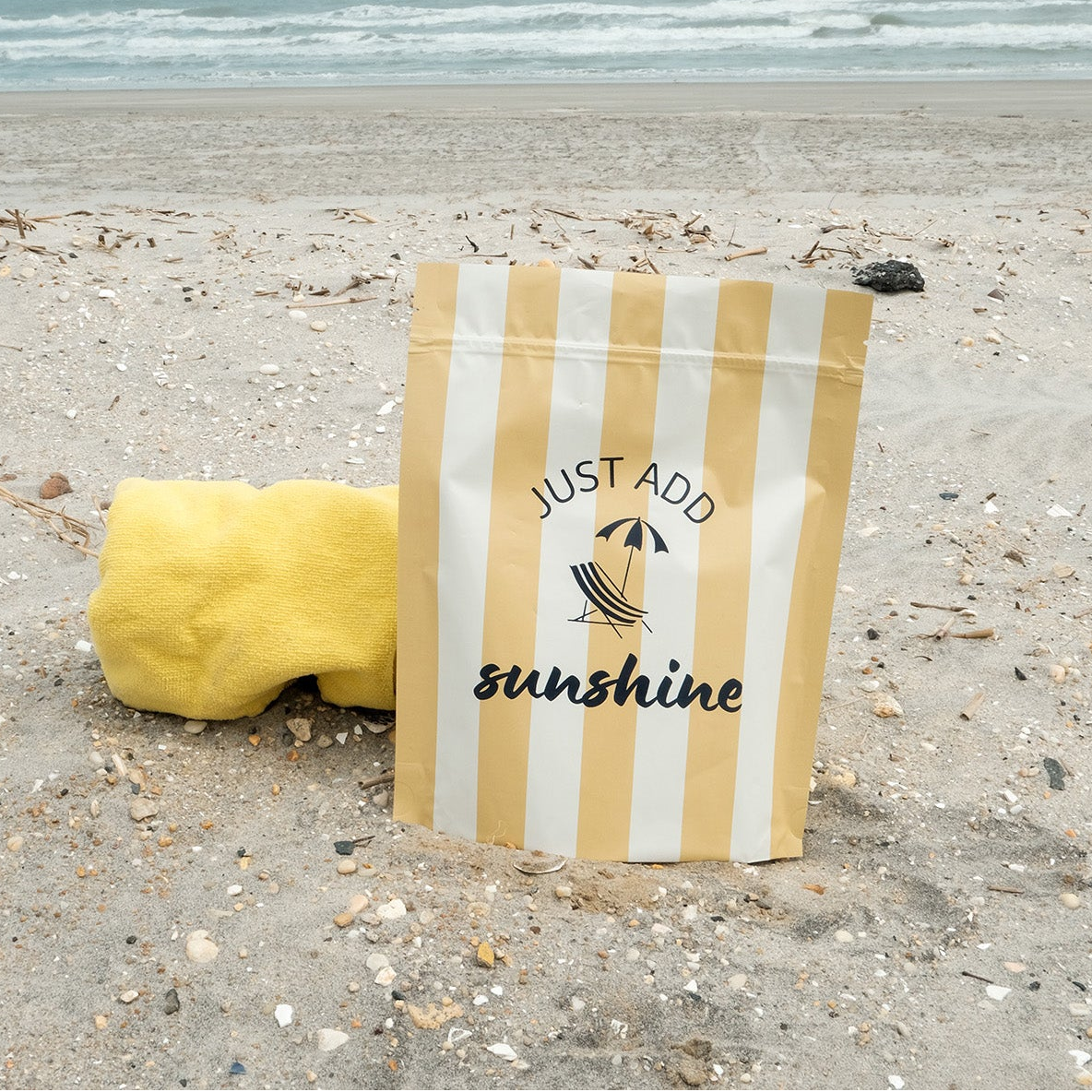 Striped bag with 'Just Add Sunshine' text on a sandy beach