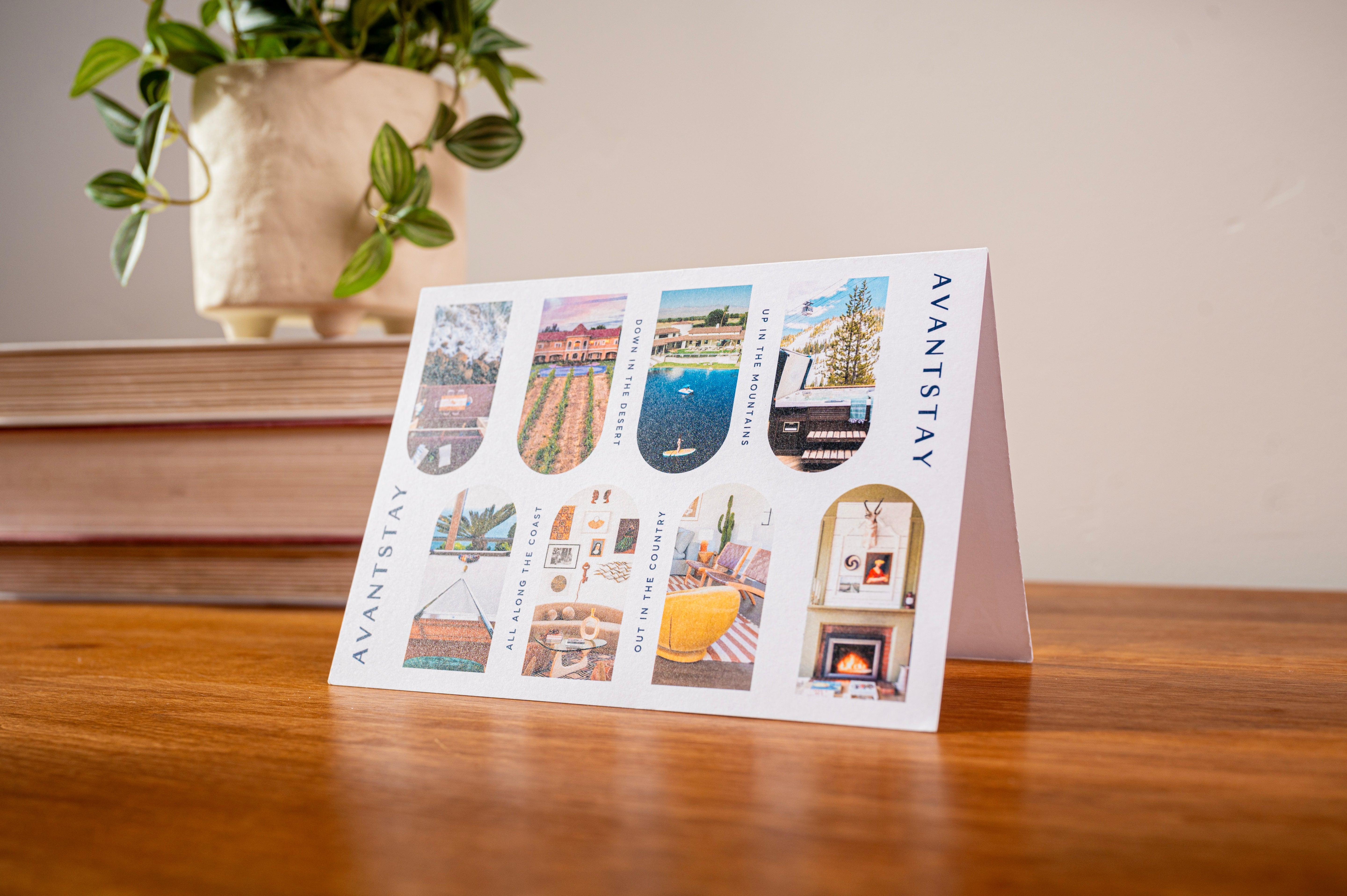 AvantStay welcome card with colorful travel images on a wooden desk near houseplant.