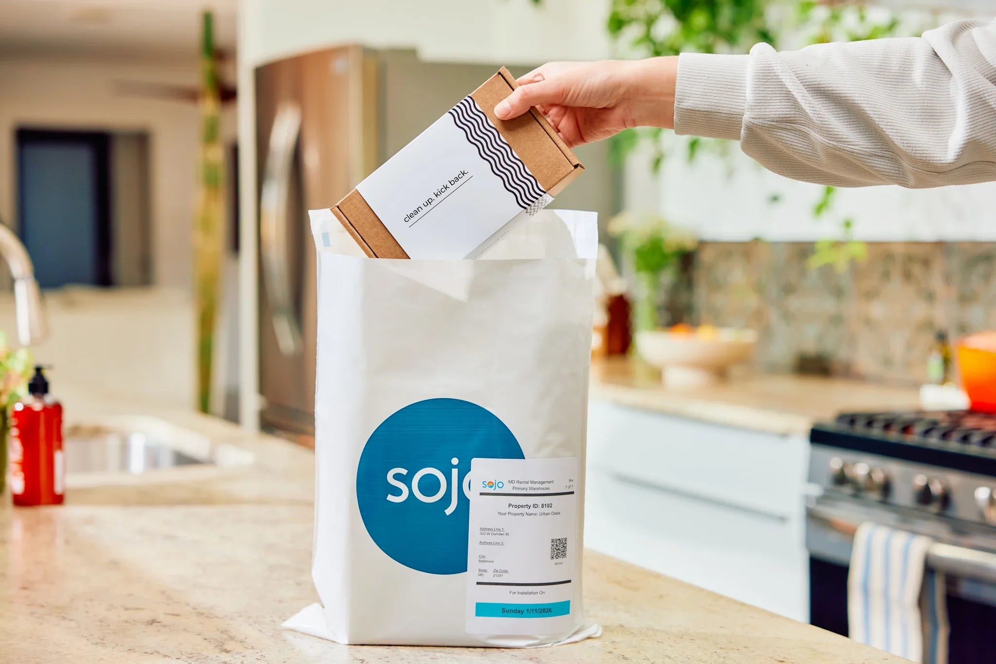 Hand placing box labeled "clean up. kick back." into SOJO bag in a kitchen.