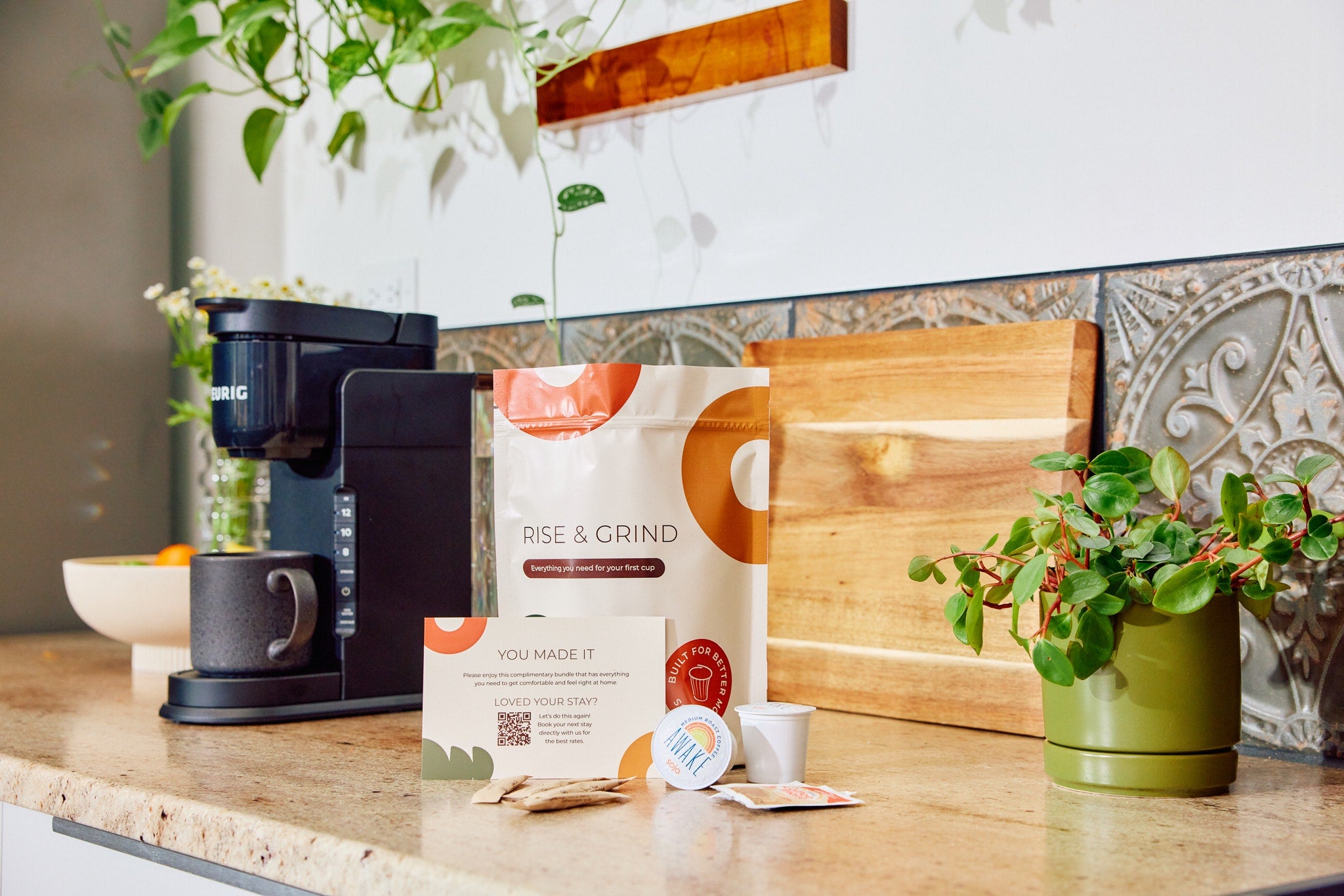 Keurig coffee maker with Rise & Grind coffee, a mug, and a small plant.