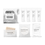 Bathroom amenities kit including shampoo, conditioner, body wash, body lotion, bar soap, hand and face soap, and makeup wipe in a bag.