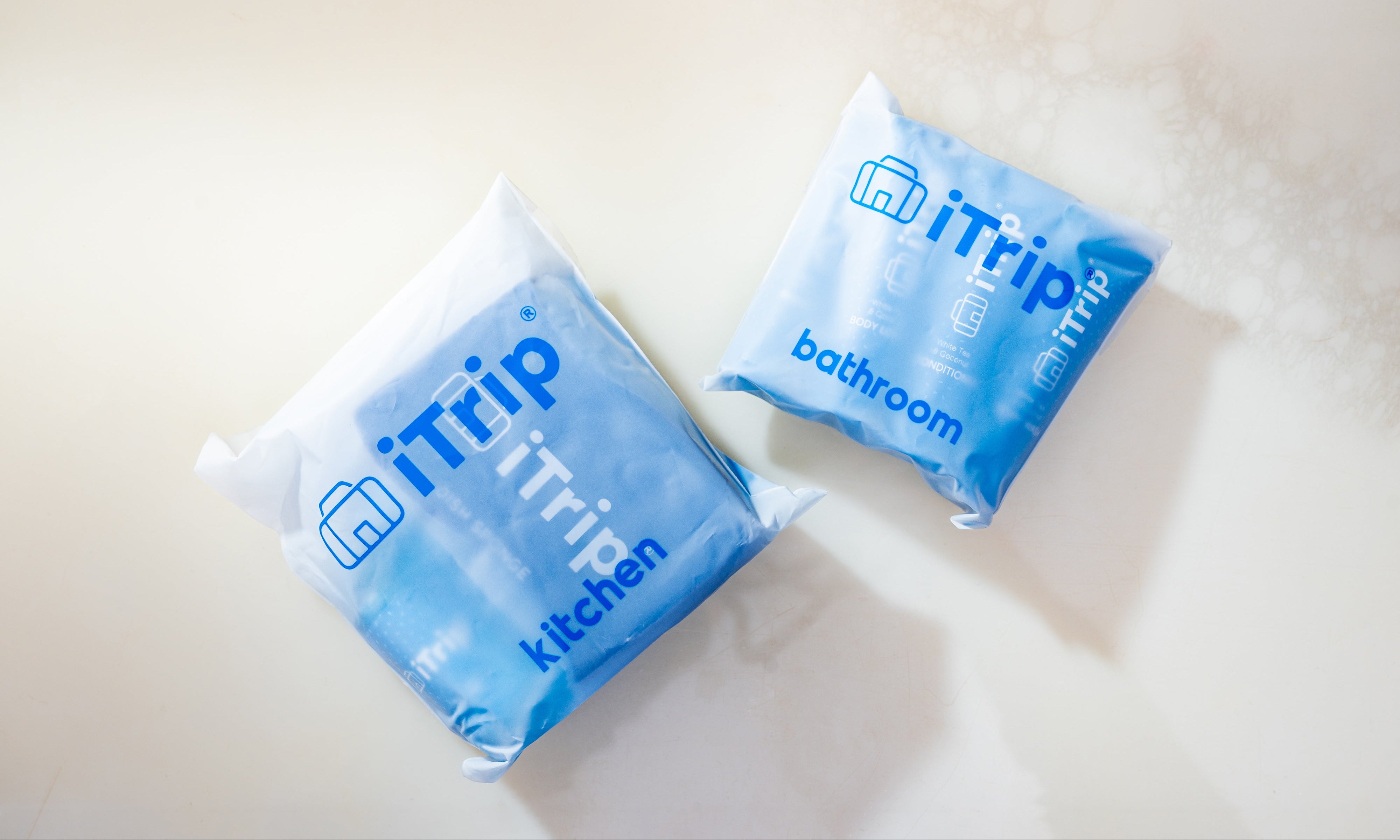 Two blue iTrip travel bags labeled kitchen and bathroom on a light surface.